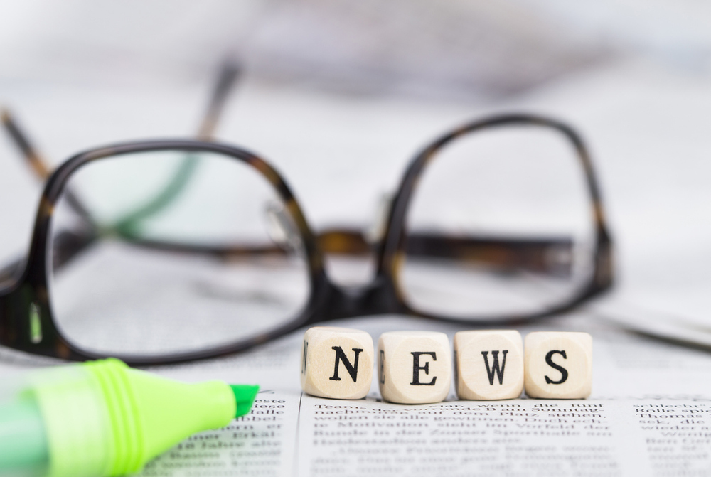 News formed by wooden letters, on top of newspapers with glasses and pen